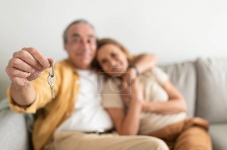 Téléchargez les photos : Concept immobilier. Couple de personnes âgées détenant les clés de la maison, embrassant et souriant, célébrant l'achat d'une propriété, déménageant dans leur propre maison, foyer sélectif - en image libre de droit