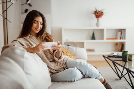 Photo for Smiling young asian woman typing on smartphone, playing game, watching video in light living room interior, free space. Application for online shopping, sale, chatting at home, ad and offer - Royalty Free Image
