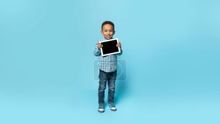 Photo for Little black boy demonstrating tablet with blank screen, recommending app or website for online education, showing copy space for your design, mockup, panorama - Royalty Free Image