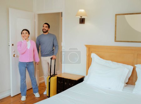 Foto de Turistas Pareja entrando en la habitación del hotel de pie con la maleta en el interior. Los cónyuges que buscan una lujosa suite disfrutando de la luna de miel. Concepto de oferta de alojamiento de vacaciones románticas y viajes - Imagen libre de derechos
