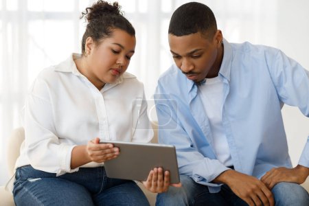 Photo for Attractive young chubby mixed race woman psychologist having conversation with male patient, showing him digital pad, explaining mental processes. Depressed black guy attending therapy session - Royalty Free Image