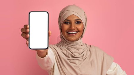 Téléchargez les photos : Jolie appli. Femme musulmane souriante dans le hijab montrant Smartphone avec écran vide à la caméra, Belle femme islamique dans le foulard Hoding téléphone portable vide dans la main, Collage, Mockup - en image libre de droit