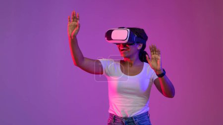 Photo for Digital World. Excited Black Woman Wearing VR Glasses Playing Video Game In Neon Light, Young African American Female Experiencing Virtual Reality While Standing Over Purple Background, Copy Space - Royalty Free Image