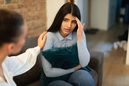 Photo for Unhappy teen lady having problem, hugging pillow and talking with friend who showing compassion and trying to appease. Friendly support in difficult time, comforting through emotional problems - Royalty Free Image