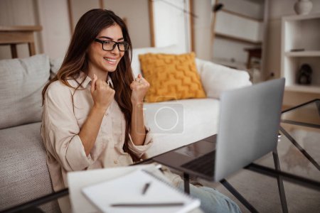 Photo for Glad smiling millennial mixed race woman in glasses has video call on laptop, making victory and success gesture in room interior. Win, great work, business remotely and study at home - Royalty Free Image