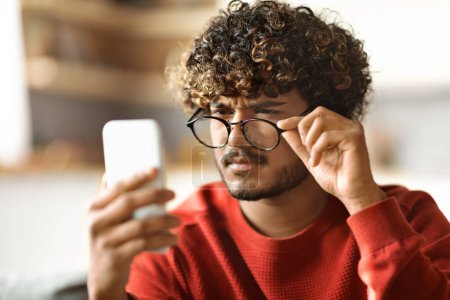 Photo for Eyesight Problems Concept. Young Indian Guy Wearing Eyeglasses Reading Message On Smartphone, Millennial Eastern Man Looking At Cellphone Screen, Taking Off Glasses And Squinting, Closeup Shot - Royalty Free Image