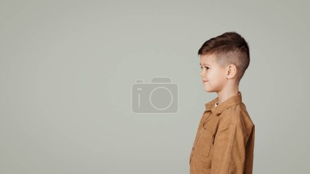 Photo for Smiling little european boy looking at empty space, isolated on gray studio background, panorama. Ad and offer for pupil, study and education at elementary school and childhood - Royalty Free Image