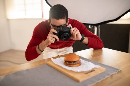 Photo for Food photographer handsome young middle eastern man wearing casual outfit and eyeglasses taking photos of delicious juicy meaty hamburger at photo studio, using dslr camera - Royalty Free Image