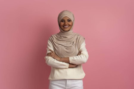 Photo for Portrait Of Confident Young Muslim Woman In Hijab Posing With Folded Arms Over Pink Background In Studio, Successful Middle Eastern Lady In Headscarf Looking And Smiling At Camera, Copy Space - Royalty Free Image