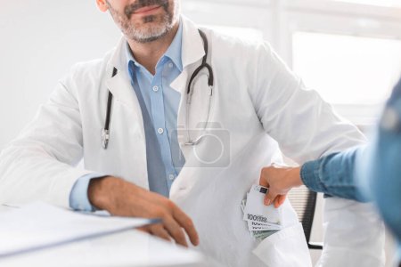 Photo for Female hand putting money in doctors pocket, general practitioner receiving cash from grateful unrecognizable patient at his office in clinic. Bribery in medicine concept - Royalty Free Image