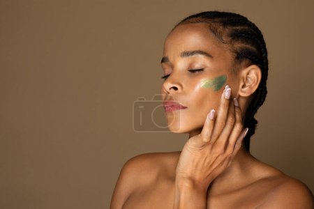 Photo for Face skin care. Black woman applying cosmetic cream on clean hydrated skin, female with natural makeup applying facial moisturizer, new beauty product or facial mask - Royalty Free Image