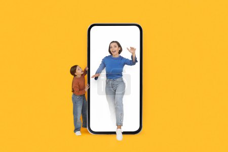 Photo for Daughter Looking At Mom Walking Out Of Big Blank Smartphone With White Screen, Mother And Female Child Posing Together Over Yellow Background In Studio, Advertising Online Offer, Collage, Mockup - Royalty Free Image
