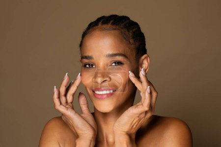 Photo for Beauty face. Happy black middle aged woman touching healthy skin and smiling, female with fresh glowing hydrated facial skin and natural makeup on brown background - Royalty Free Image