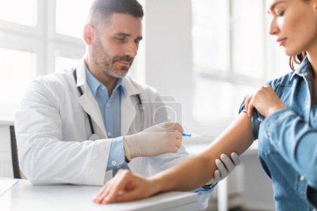 Photo for Young lady getting vaccinated against coronavirus, middle aged male doctor making injection in shoulder for female patient, clinic interior, closeup, copy space - Royalty Free Image