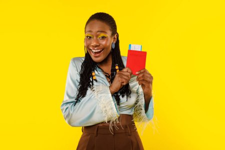Téléchargez les photos : Voyage de vacances. Joyeuse dame afro-américaine tenant passeport et carte d'embarquement posant sur fond jaune studio, souriant à la caméra. Publicité Touristique Féminine Billets Bon Marché Concept - en image libre de droit
