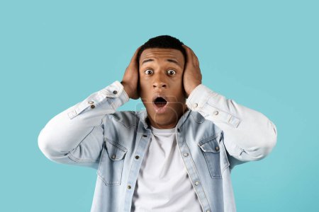 Photo for Shocked frightened millennial black guy in casual with open mouth holding head his hands isolated on blue studio background. Human emotions, facial expression, fear, reaction to bad news - Royalty Free Image