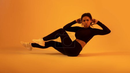 Photo for Fitness workout. Black sportswoman in fitwear doing elbow to knee abs crunch exercising on neon orange sudio background. Athletic lady flexing abs muscles. Sport and bodybuilding - Royalty Free Image