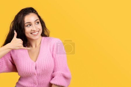 Photo for Happy young caucasian brunette woman showing phone sign with hand, look at free space, isolated on yellow studio background. Flirt, communication, people emotions, call me back - Royalty Free Image