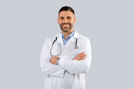 Téléchargez les photos : Santé, concept du personnel médical. Portrait d'un médecin souriant posant les bras croisés sur fond de studio gris, espace libre. Médecin généraliste professionnel. - en image libre de droit
