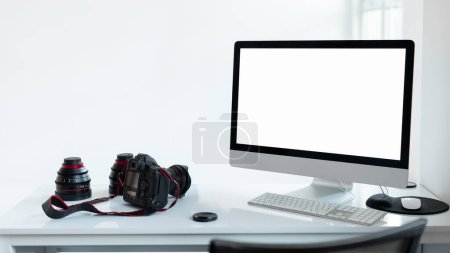 Foto de Lugar de trabajo del fotógrafo con monitor de computadora de pantalla en blanco y accesorios de cámara, fondo de estudio blanco, plantilla de maqueta para su diseño - Imagen libre de derechos