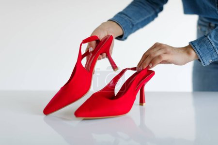 Foto de Mujer tocando y colocando zapatos rojos sobre fondo claro en photostudio, directora de arte femenina trabajando con nueva colección durante el rodaje de moda - Imagen libre de derechos