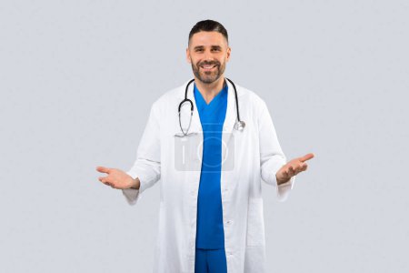 Photo for Portrait of friendly male doctor in uniform talking and gesturing at camera, consulting patient, posing on grey background and smiling, copy space - Royalty Free Image