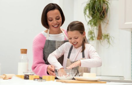 Photo for Happy caucasian young mother and teen daughter in aprons make dough for cookies with hands, have fun in minimalist kitchen interior. Cook food together, homemade sweets at home - Royalty Free Image