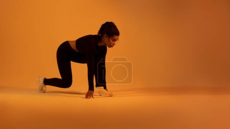 Photo for Fit black sportswoman doing crouch start ready for running on neon orange studio background, panorama, copy space. Shot of young female runner - Royalty Free Image