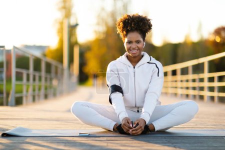 Téléchargez les photos : Jeune afro-américaine sportive pratiquant le yoga en plein air, Belle femme noire étirant les muscles des jambes, Faire l'exercice extensible papillon tout en faisant de l'exercice de remise en forme à l'extérieur, Copier l'espace - en image libre de droit