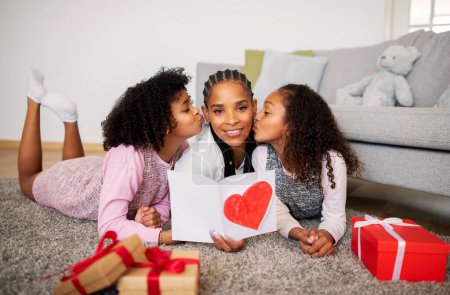 Photo for African American Preteen Girls Kissing Mom Congratulating Her On Mothers Day Lying On Floor At Home. Young Mommy Smiling To Camera Receiving Gifts From Kids Celebrating Family Holiday Together - Royalty Free Image