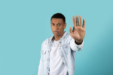 Foto de Triste enojado serio confiado millennial negro chico en casual mostrando mano stop signo aislado en fondo de estudio azul, espacio de copia. Lucha contra la discriminación, prohibición de conflictos, intimidación - Imagen libre de derechos