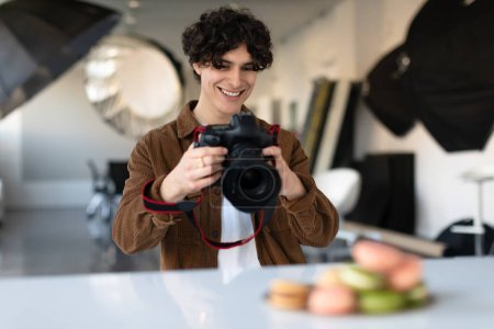 Photo for Male food photographer taking photos of delicious sweets macarons at modern photostudio, using dslr camera and working with lighting equipment - Royalty Free Image
