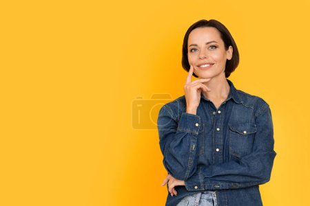Photo for Portrait Of Beautiful Middle Aged Woman Posing Over Yellow Background In Studio, Smiling Attractive Female Wearing Denim Shirt Touching Face And Looking At Camera, Closeup With Copy Space - Royalty Free Image