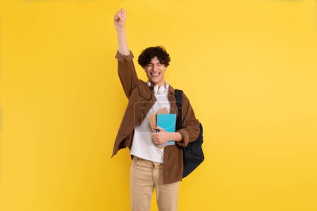 Photo for Joyful Male Student Gesturing Yes Posing With Eyes Closed Holding Backpack And Notebooks Standing On Yellow Studio Background. Guy Celebrating Educational Luck. Successful Admission To University - Royalty Free Image