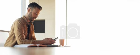 Photo for Serious european adult businessman typing on phone at workplace in office or home interior with window, free space, sun flare. Communication remotely, business, work with device - Royalty Free Image