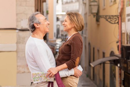 Téléchargez les photos : Conjoints aînés souriants étreignant debout sur une rue dans la ville européenne à l'extérieur. Aimer couple retraité profiter de vacances romantiques à pied à l'extérieur. Offre de voyage à la retraite Concept - en image libre de droit