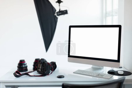 Photo for Workplace of photographer with empty computer screen and camera accessories, modern photostudio with lighting equipment, mockup template for your design - Royalty Free Image