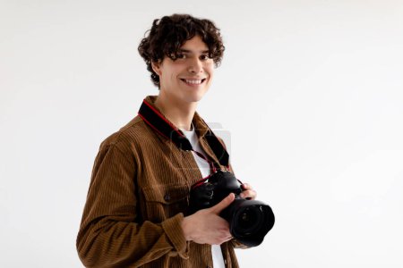 Téléchargez les photos : Portrait de photographe professionnel masculin avec appareil photo numérique moderne debout dans un studio photo sur fond blanc, regardant et souriant à l'appareil photo, espace libre - en image libre de droit