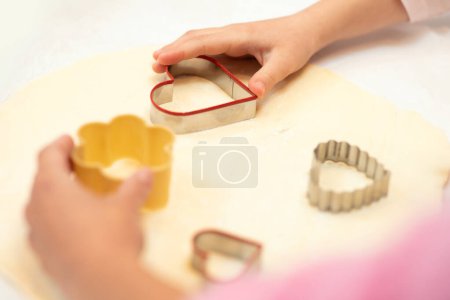 Photo for Hands of caucasian young mom and little daughter make cookie from dough with forms on kitchen table, close up. Tasty homemade food, hobby at free time, cooking sweets together at home - Royalty Free Image