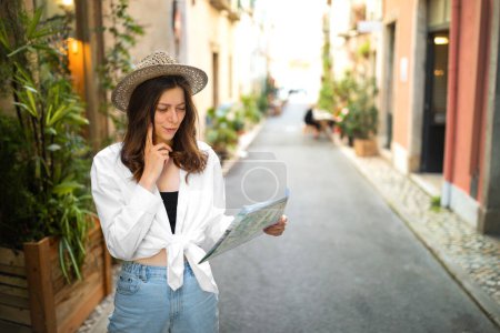 Téléchargez les photos : Concentré sérieux jeune femme caucasienne décontractée et chapeau regardant la carte, rechercher hôtel, profiter de voyager dans la nouvelle ville, à l'extérieur. Aventure, voyage seul, vacances et voyage en été - en image libre de droit