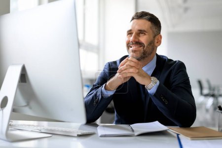Téléchargez les photos : Heureux cher homme d'affaires d'âge moyen en costume assis devant l'ordinateur, pensant et souriant, travaillant au bureau au bureau. Homme entrepreneur détournant les yeux, considérant les idées d'affaires, espace libre - en image libre de droit