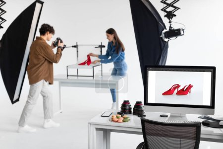 Téléchargez les photos : Photographe homme et directrice artistique femme prenant des photos de chaussures rouges, travaillant ensemble dans un photostudio moderne, faisant des séances photo de contenu, se concentrer sur le moniteur avec photo - en image libre de droit