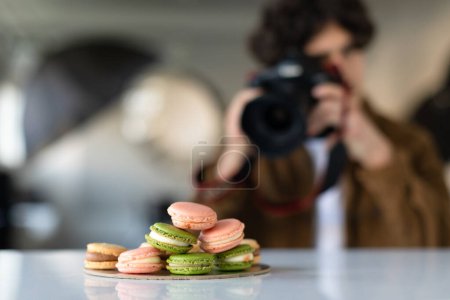 Photo for Young man with professional camera taking food photo in photostudio, photographer working and taking pictures of macarons, selective focus on sweets - Royalty Free Image