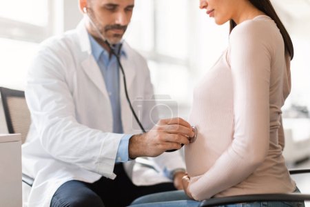 Photo for Healthcare and prenatal care concept. Male doctor examining pregnant womans belly using stethoscope, listening babys heartbeat in office at maternity hospital, cropped - Royalty Free Image