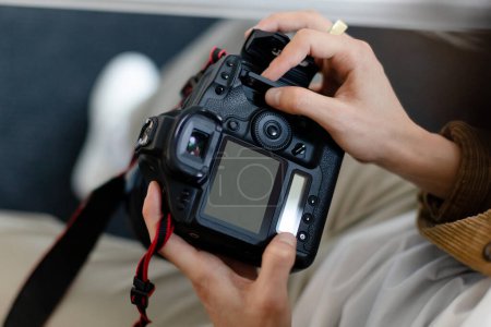 Photo for Rear view of male photographer holding camera working with photos, looking through taken pictures, blank empty screen mockup. Art and creative profession concept - Royalty Free Image