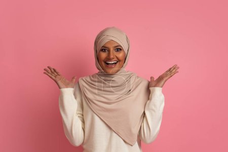 Foto de ¡Vaya! Mujer musulmana sorprendida en hijab abriendo la boca y levantando las manos con asombro mientras estaba de pie sobre el fondo del estudio rosa, emocionada mujer árabe reaccionando emocionalmente a las grandes ventas, espacio de copia - Imagen libre de derechos