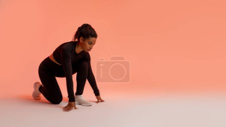 Photo for Motivated african american female runner, standing in crouch start position, ready for race over peach neon background, panorama. Fit black lady in fitwear preparing for running, free space - Royalty Free Image