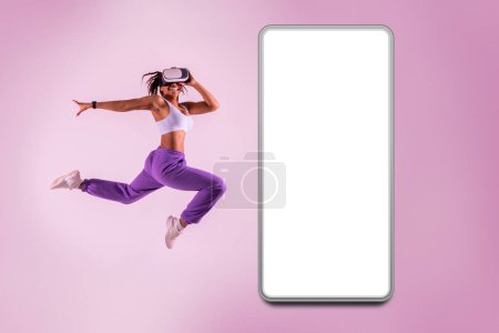 Photo for Active african american lady experiencing the metaverse in virtual reality headset near huge smartphone with blank screen, mockup, pink neon background - Royalty Free Image
