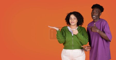 Photo for Positive cheerful beautiful young interracial couple handsome black guy and pretty chubby hispanic woman showing free space for advertisement, isolated on red studio background, web-banner - Royalty Free Image