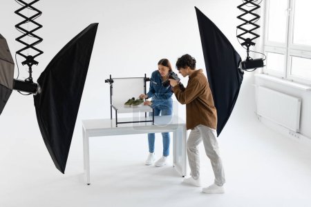 Équipe professionnelle de photographe et de gestionnaire de contenu tirant des chaussures élégantes en photostudio, travaillant ensemble, pleine longueur prise de vue, espace libre